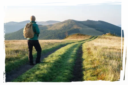 Mann mit Rucksack blickt in die Ferne auf einem Weg durch die Natur – Symbol für persönliche und berufliche Veränderung