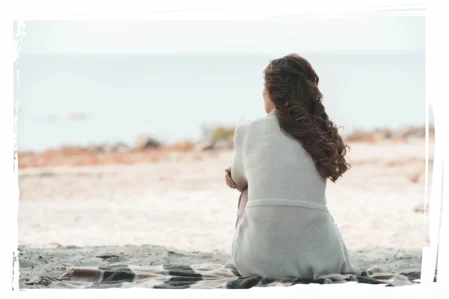 Frau sitzt am Strand und blickt nachdenklich aufs Meer